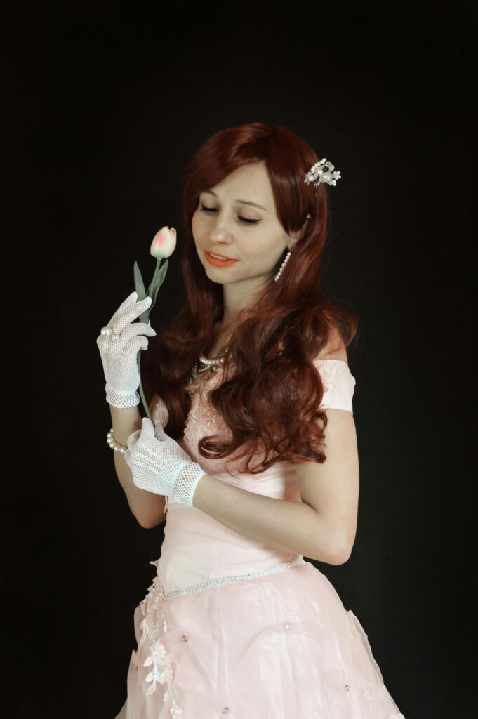 A woman in a pink dress gracefully holds a tulip against a black background, exuding elegance.